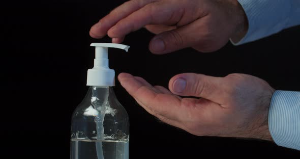 Man Push Dispenser and Liquid Soap Squeezed Out To Hand, Black Background. 