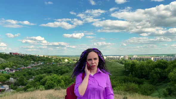 Young beautiful woman talking on mobile phone, standing in hilly terrain.