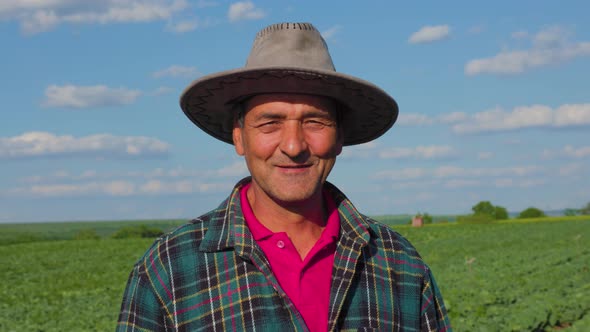 The Portrait of a Male Farmer in a Plaid Shirt with a Hat on His Head is Satisfied