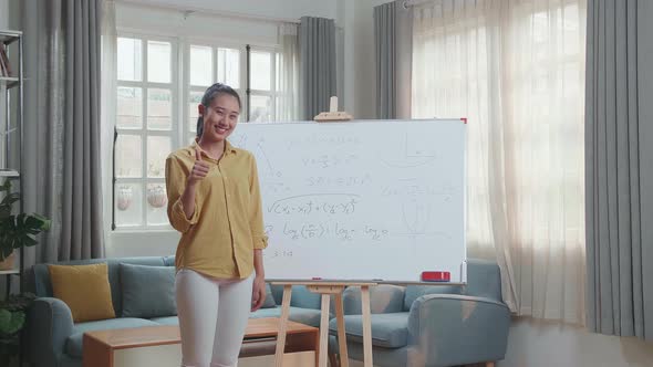 Smiling Asian Female Teacher Showing Thumbs Up Gesture To Camera While Teaching Math At Home