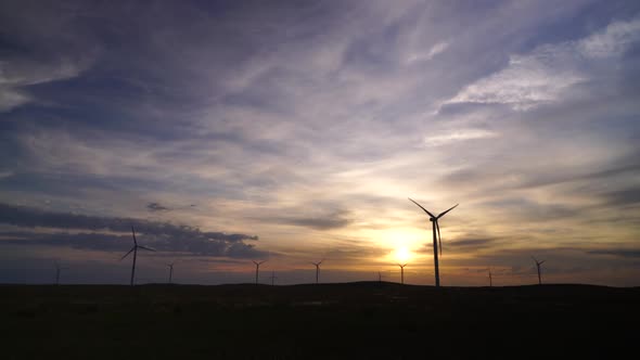 Motion the Blades of a Large Wind Turbine in a Field Against a Background of Orange Sunset on the