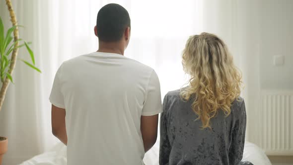 Happy Relaxed Interracial Couple Sitting on Bed Head to Head Looking at Each Other Smiling