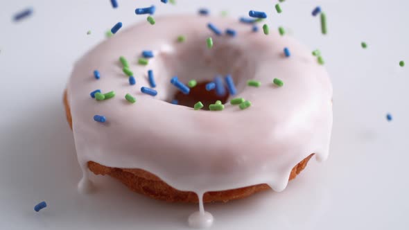 Sprinkling candy chocolate on frosted doughnut. Slow Motion.