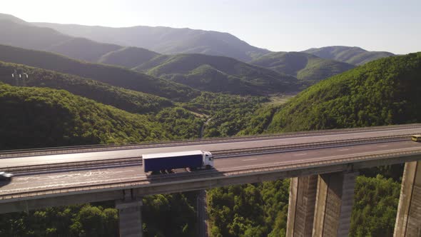 Aerial View of Highway Viaduct with Truck Driving in Sunny Day Against Green Hills