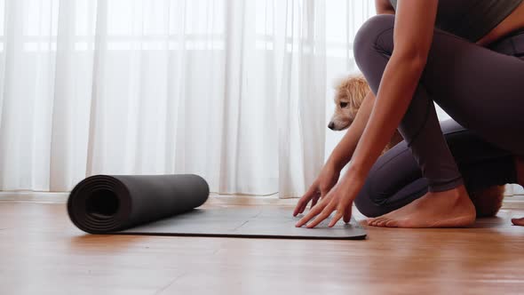 young Asia woman unrolling roll black yoga mat for playing yoga with her dog at home