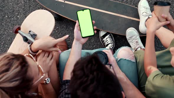 Young Millennial Friends Sitting Outside with Coffee and Looking at Green Screen Phone in Park