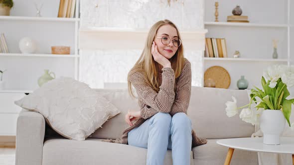 Happy Young Caucasian Mom Blonde Woman in Glasses Nanny Sits on Sofa in Living Room Looks at Little