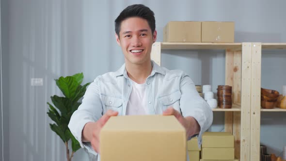 Portrait of Asian handsome man handing package to customer in store and looking at camera.