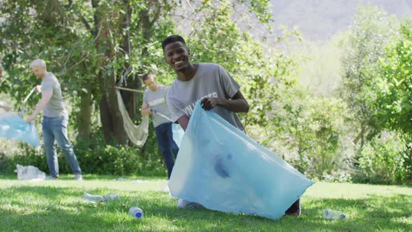 Happy diverse group of friends in volunteer t shirts putting plastic waste in refuse sacks outdoors