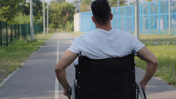 Back View Anonymous Young Man Rides Wheelchair Using Hands on Summer Stadium Track Person Prepares