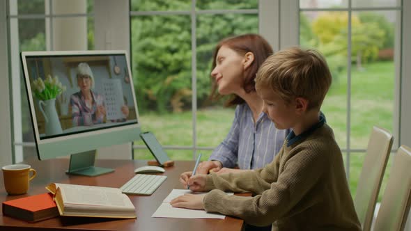 Young 30s Mother Helping Her Son with Online Lesson at Home