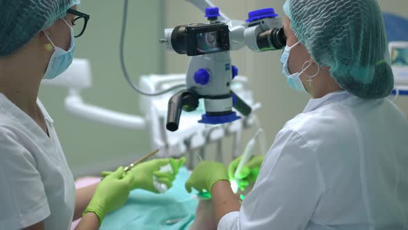 Concentrated Dentist Examining Tooth Hole with Dental Microscope As Assistant Passing Tools in Slow