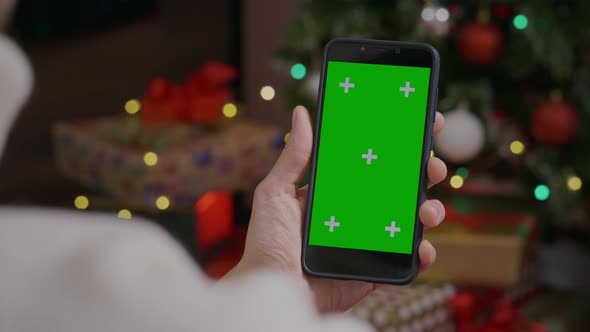 Close-up shot of green screen template smartphone in female hands in Christmas interior at home