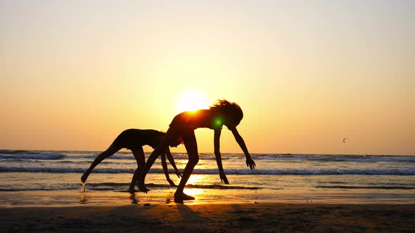 Silhouette of Sporty Young Women Practicing Acrobatic Element on the Beach