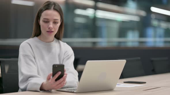 Woman Working on Smartphone and Laptop in Office