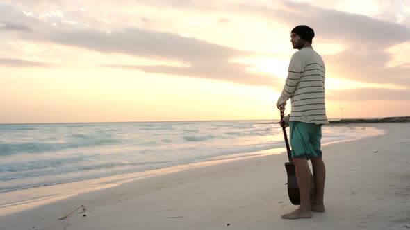 Young Beautiful Man Stands Up Looking to Ocean at Beach Seaside at Sunrise or Sunset in Summer