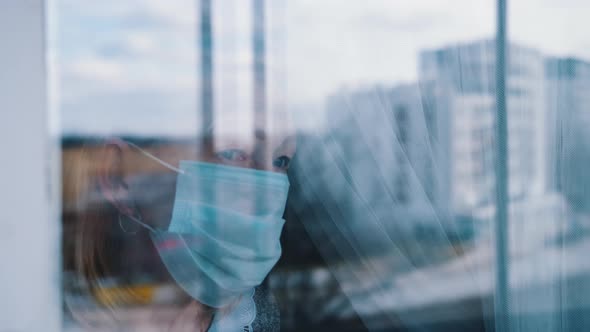 Portrait of Lonely Elderly Woman in Quarantine with Face Mask Looking Through the Window