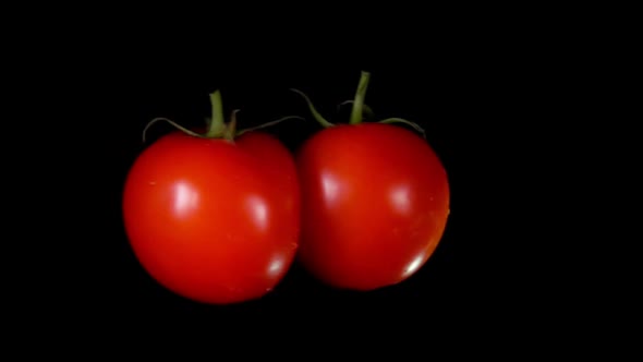 Two Ripe Red Tomatoes are Flying to Each Other Colliding on a Black Background
