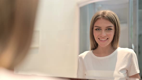 Rear View of Young Woman Looking in the Mirror and Smiling