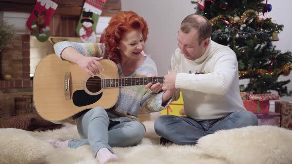 Cheerful Caucasian Husband Teaching Positive Wife Playing Guitar on New Year's Eve