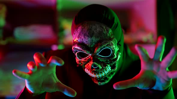 a Man in a Scary Glowing Death Mask Moves Arms and Swings in a Neon Flashing Light