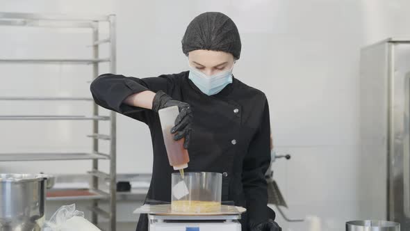 Front View of Beautiful Concentrated Woman in Covid19 Face Mask Pouring Liquid Pastry Syrup on Baked