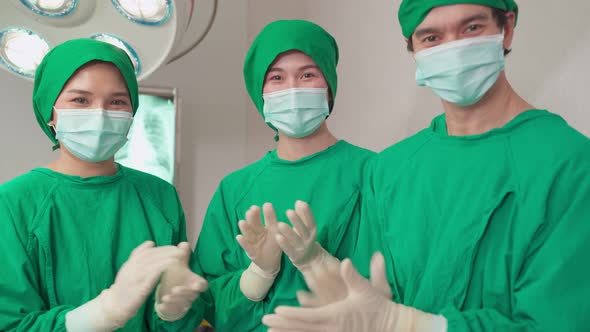 Group of Asian doctors remove mask, working in Hospital operating room with success and clap hands.