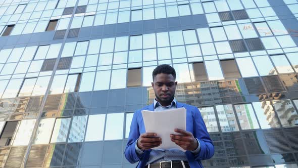 African American Realtor Checks Information in Paper Document Against Office Building