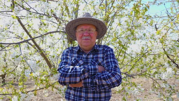 Portrait of Old Male with Hat in Orchard in Spring Arms Crossed