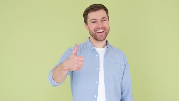 Young Handsome Man with Beard in Denim Shirt on Yellowgreen Background Smiling and Happy Thumb Up