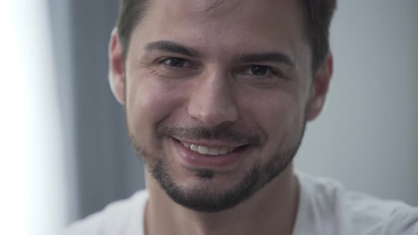 Portrait of Handsome Smiling Man in White T-shirt Sitting at Home Smiling While Looking