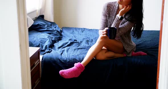 Thoughtful woman having coffee on bed