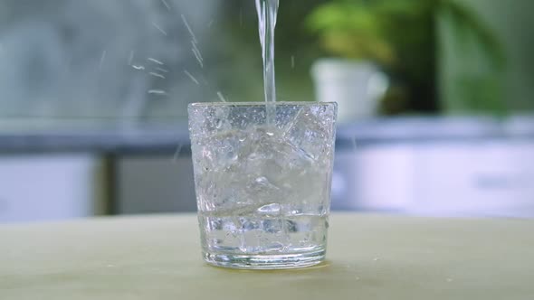 Pure Clear Mineral Water is Poured Into a Glass with Ice Cubes