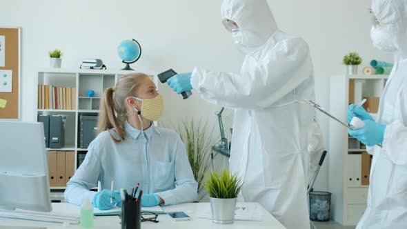 People in Protective Costumes Checking Body Temperature in Office with No-touch Thermometer alt