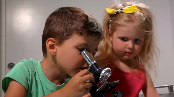 Llittle Boy is Sharing a Microscope with a Cute Little Girl in a White Classroom