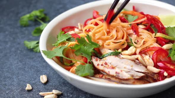 Eating Pad Thai Noodles with Chicken, Peanuts and Vegetables in Bowl, Dark Background.