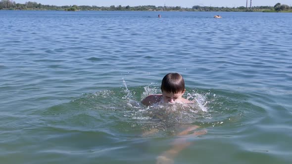 Happy Child Swimming Splashing Jumping on the Beach in Water in Sunlight