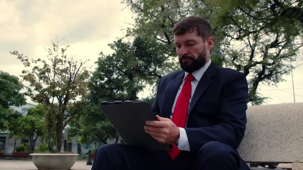 Serious Elegant Bearded Man in an Expensive Suit Reads a Newspaper on a Tablet Computer While