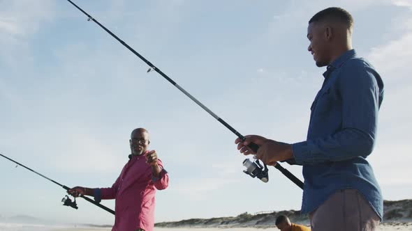 African american senior father and two teenage sons standing on a beach fishing and talking