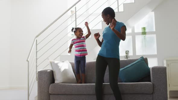 Happy african american mother and daughter dancing and having fun at home