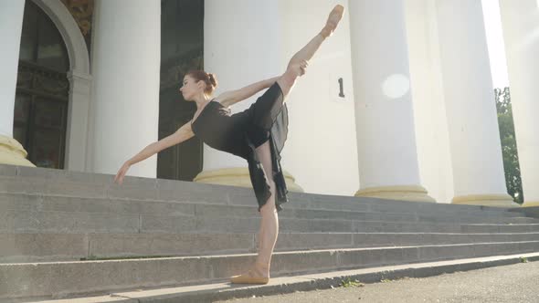 Slim Elegant Confident Ballet Dancer in Black Dress Standing on One Leg in Sunrays Outdoors