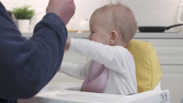 Father Feeding His Baby in the Kitchen at Home Closeup of Oneyearold Baby Boy in White High Baby