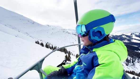 Smiling Boy with Ski Going Up on Chairlift in Mountains