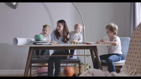 Three Blond Children Sitting at the Table with Brunette Young Mother, Talking and Smiling. Big