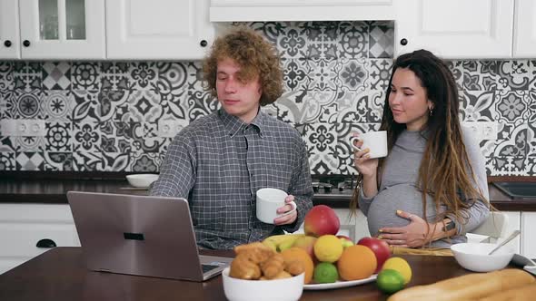 Family which Drinking Tea in Modern Kitchen and Simultaneously Using Laptop