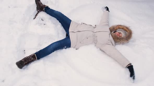 A Woman in a White Jacket Lies in the Snow Raises Her Hands Up and Down