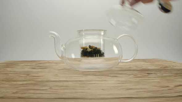 Dry White Tea in Transparent Teapot Male's Hand Covers the Pot with a Lid