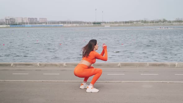 A brunette woman in an orange top and leggings is engaged in fitness. Athletic, muscular woman goes