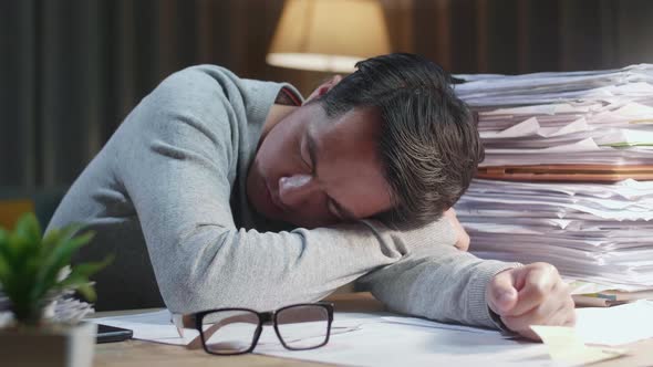 Close Up Of Tired Asian Man Sleeping Due To Working Hard With Documents At Home