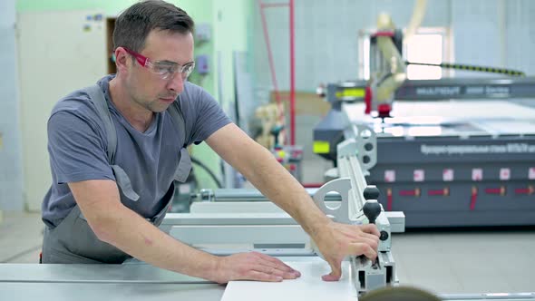 A man works in the assembly shop on a circular saw, neglecting safety